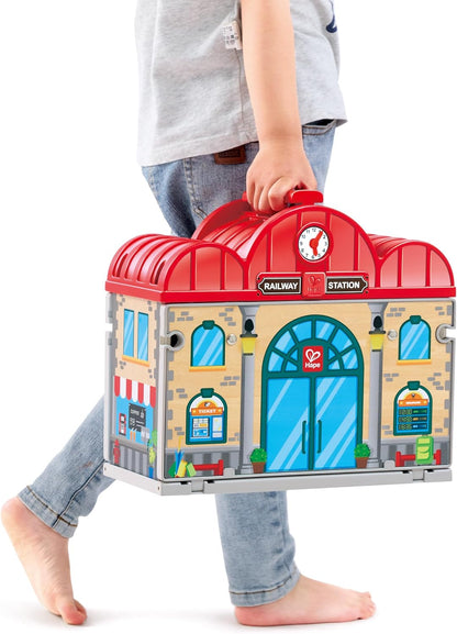 Child holding a toy train station set against a white background