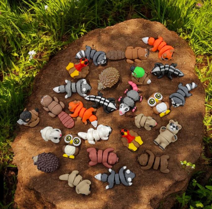 Assorted animal-shaped toys arranged on a rock in a natural setting.
